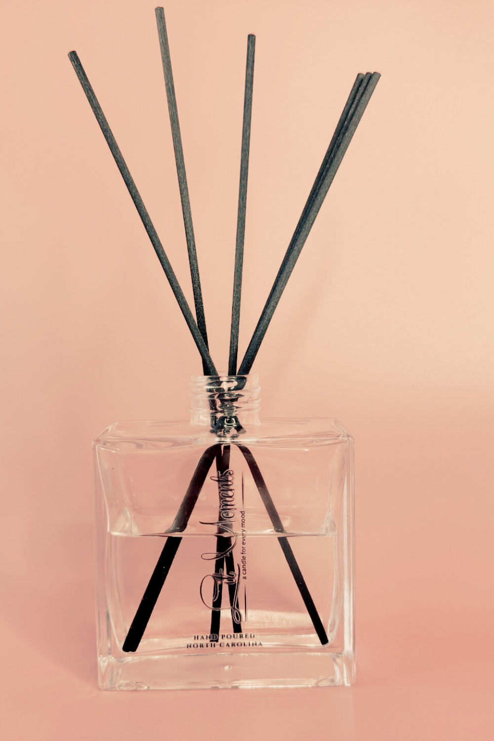 Clear diffuser bottle with black sticks on a pink background